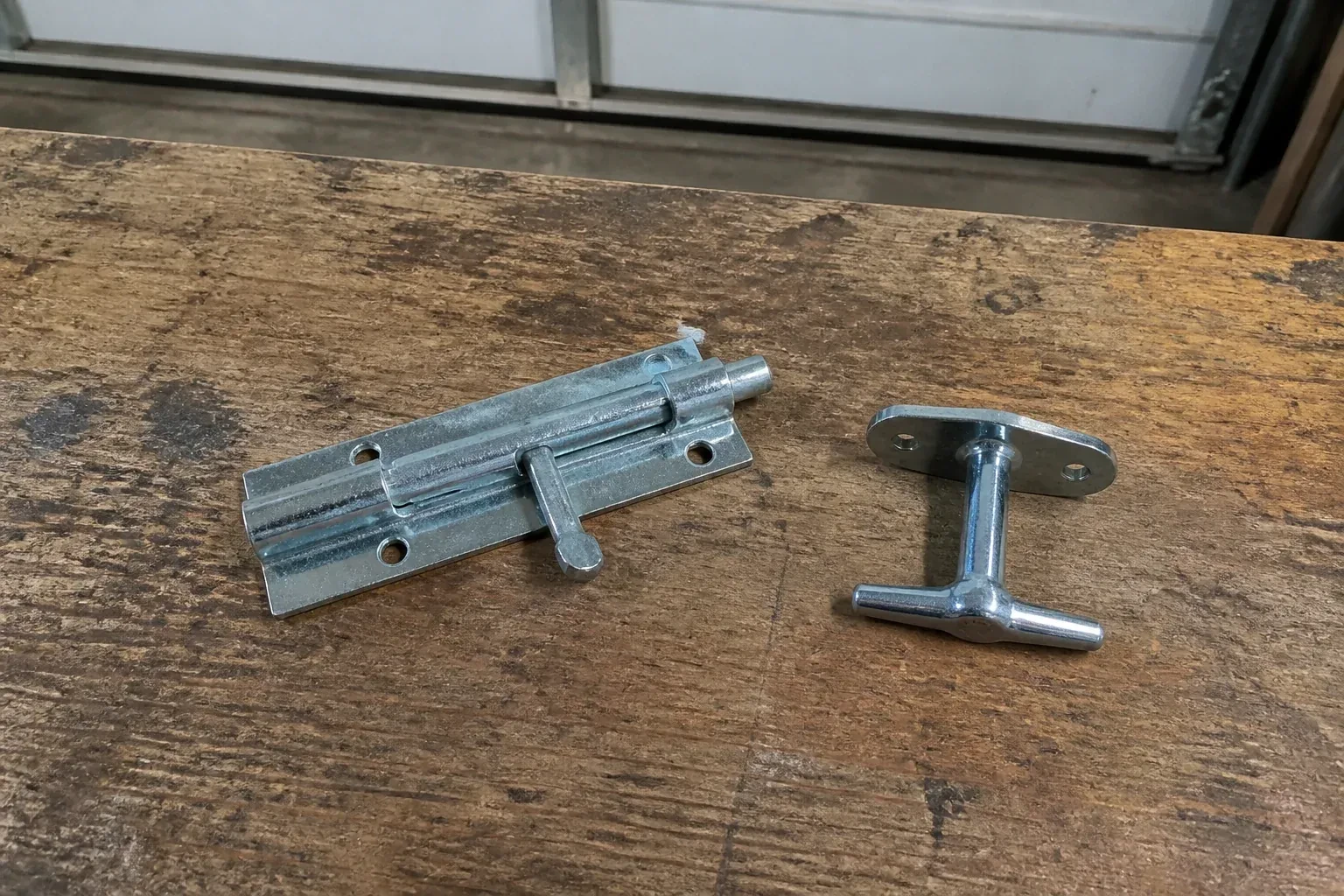Detached slide bolt and T-handle on a wooden garage workbench. — Garage Door Manual Lock Repair, Oshawa